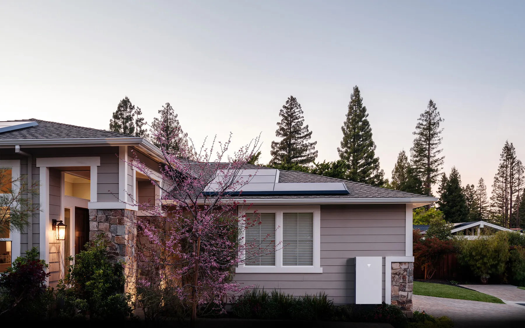 Tesla Powerwall 3 wall-mounted beside a single-storey home with rooftop solar at dusk